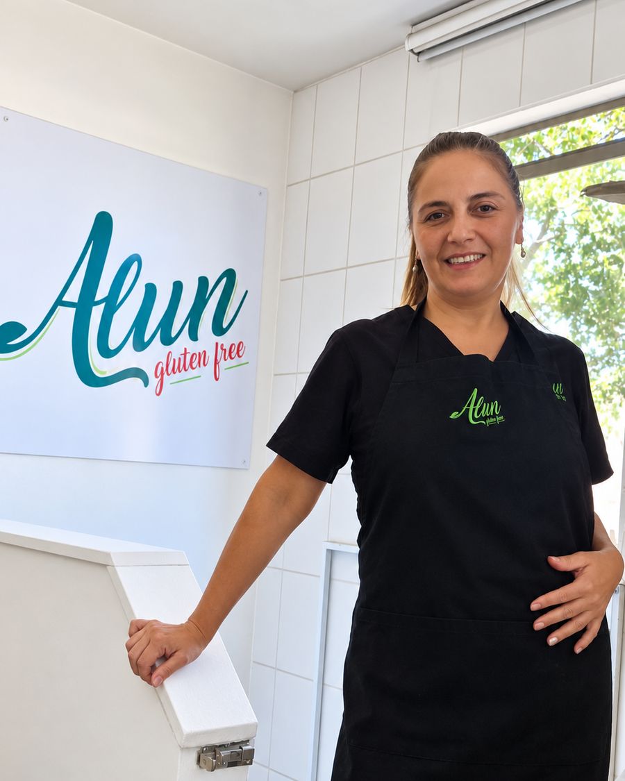 La fundadora de Alun sonriendo junto al letrero de la marca en la planta, con el delantal de Alun puesto